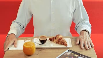Une personne assise à une table, devant un croissant, une tasse de café et un verre de jus d’orange.