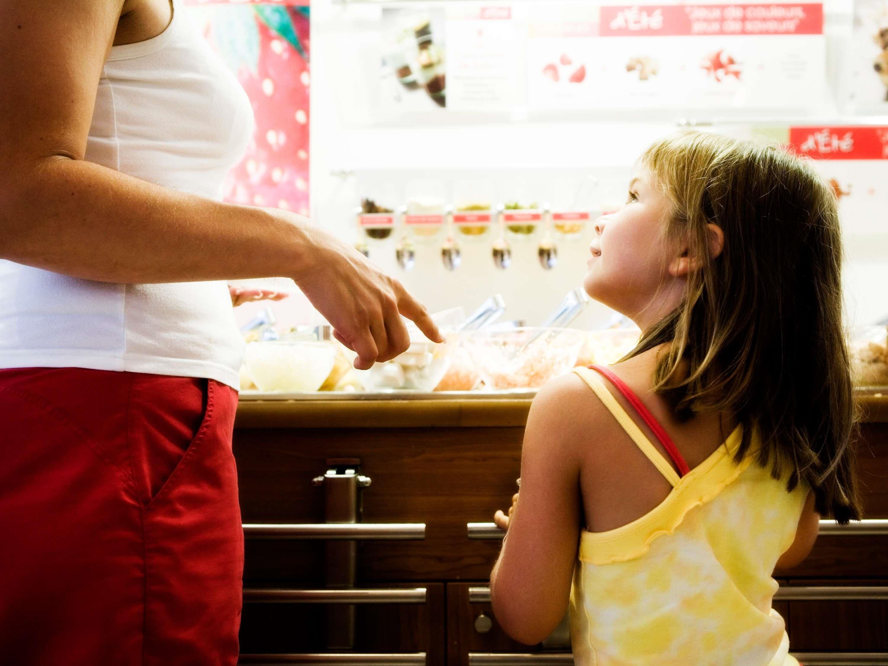 A person in a white top and red pants standing at a counter with a child in a yellow top.
