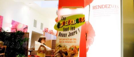 A restaurant interior with a promotional poster, wooden furniture, and a potted plant.