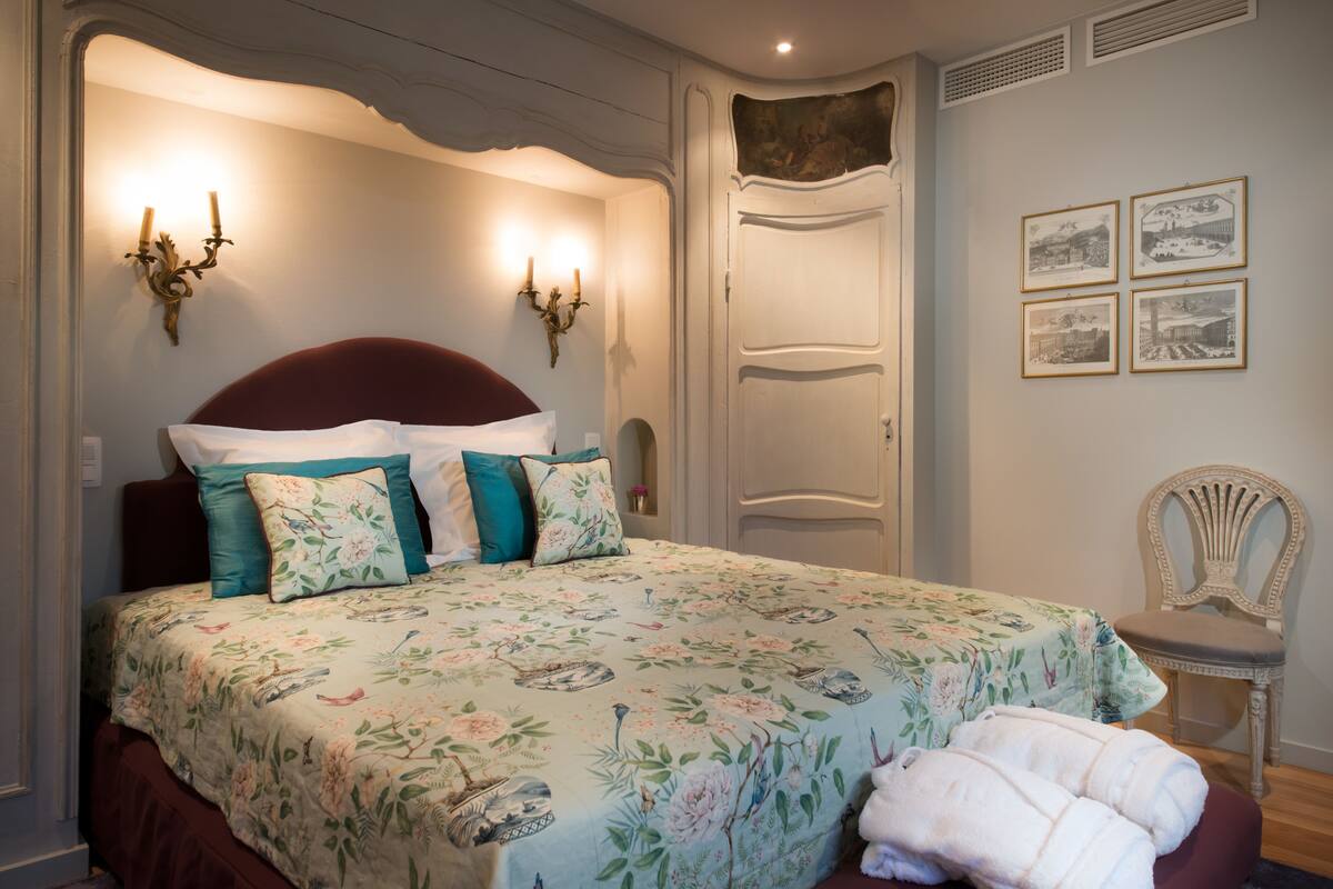 Een slaapkamer met een bloemenbedekker, een rode hoofdbord en een witte stoel.