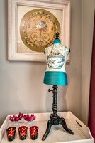 Un maniquí con un vestido de estampado azul y blanco, una lámpara de estilo vintage y tres candelabros rojos sobre una bandeja blanca.