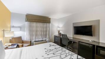 A hotel room with a bed, a desk, a television, a mini-fridge, and a window with curtains.