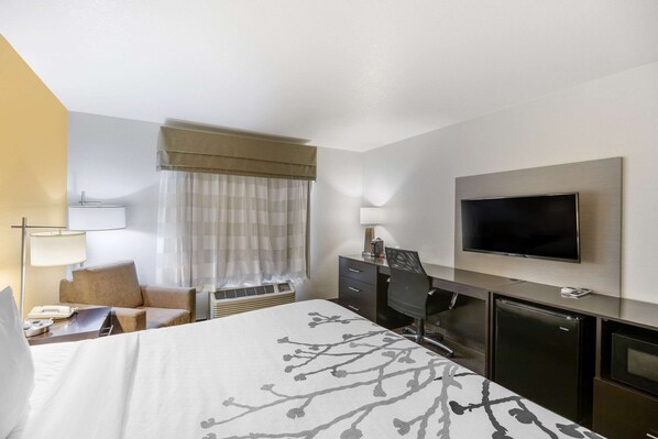 A hotel room with a bed, a desk, a television, a mini-fridge, and a window with curtains.