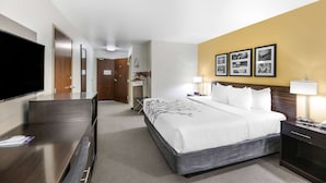 A hotel room with a bed, bedside table, lamp, TV, and a wall with framed pictures. - Sleep Inn & Suites Carlsbad Caverns Area (Carlsbad)