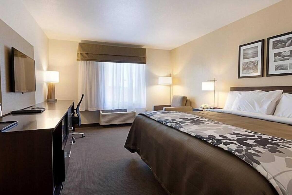 A hotel room with a bed, bedside tables, a desk, a chair, a TV, and a window with curtains.