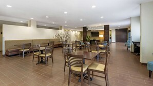 A spacious indoor area with multiple seating arrangements including tables and chairs, a sofa, and a television screen. - Sleep Inn & Suites Carlsbad Caverns Area (Carlsbad)