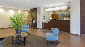 A reception area with a reception desk, two blue chairs, a potted plant, and a modern interior design. - Sleep Inn & Suites Carlsbad Caverns Area (Carlsbad)