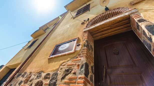 A building with a stone facade, a wooden door, and a sign indicating a restaurant. - Faunele (Orosei)