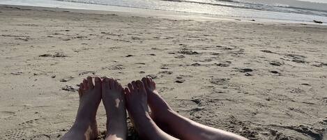 Escena de playa con las piernas y los pies de una persona descansando sobre la arena, mirando al océano.