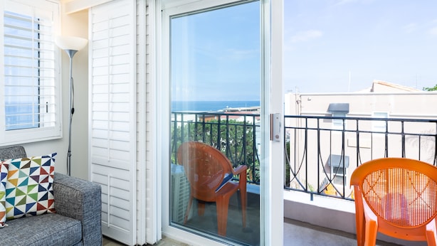 A balcony with a sliding glass door, a grey sofa with a colorful cushion, and an orange chair.