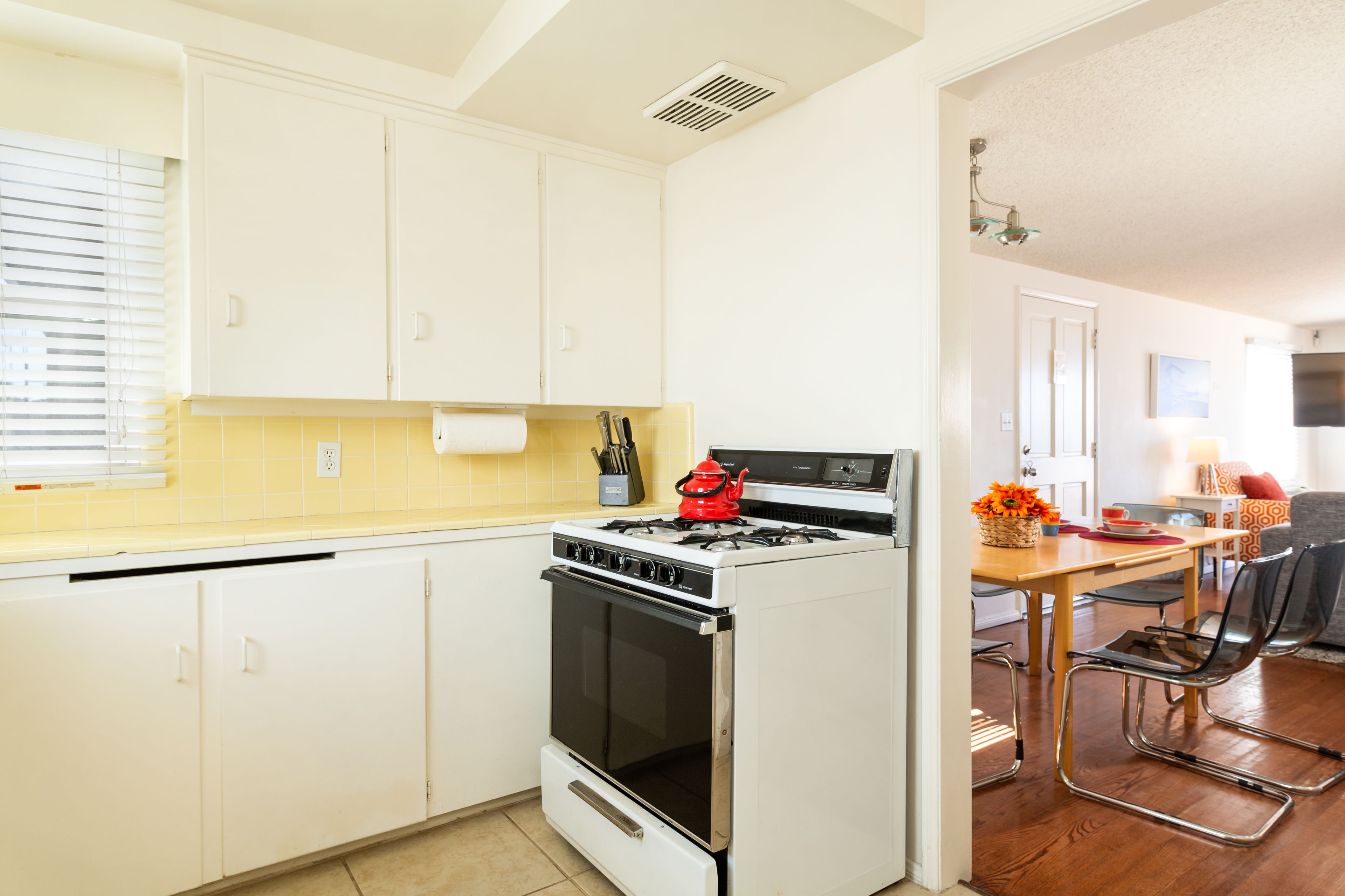 A kitchen with white cabinets, a stove, and a dining area with a table and chairs.