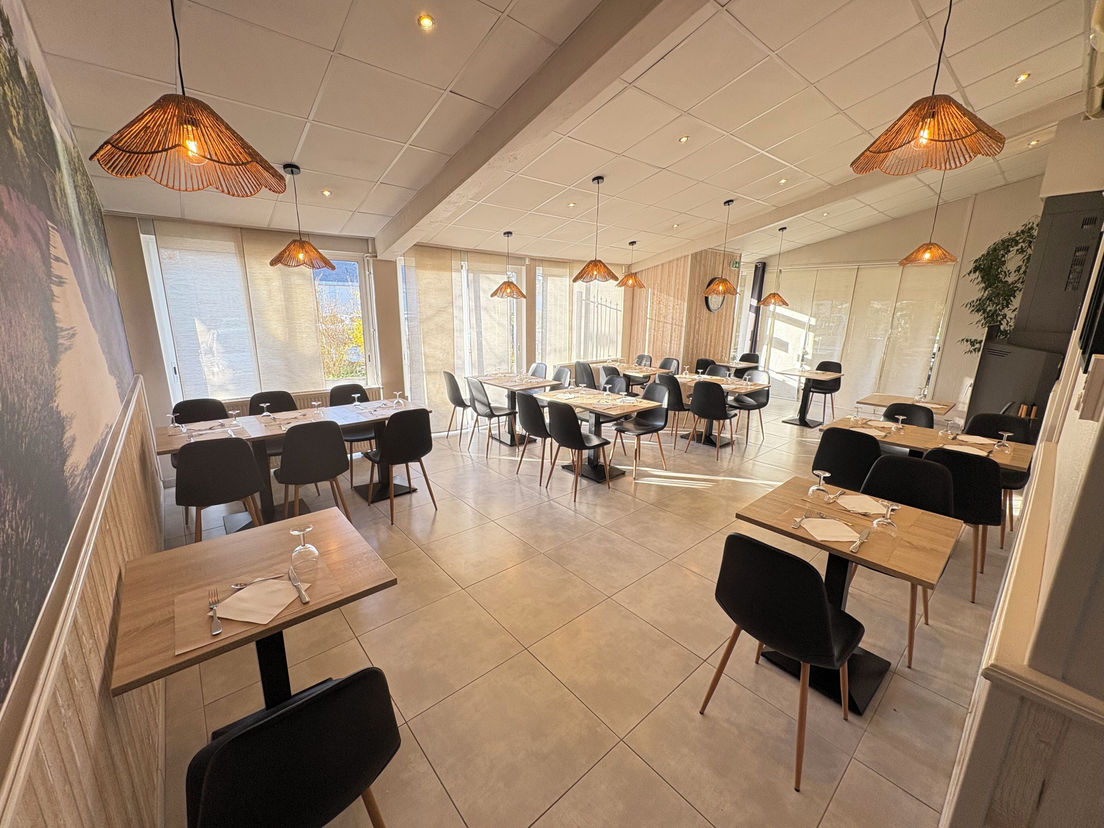 A spacious dining area with multiple tables and chairs, large windows allowing natural light, and hanging pendant lights.