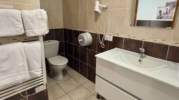 Une salle de bain équipée de toilettes, d’un lavabo, d’un porte-serviettes et d’un miroir.