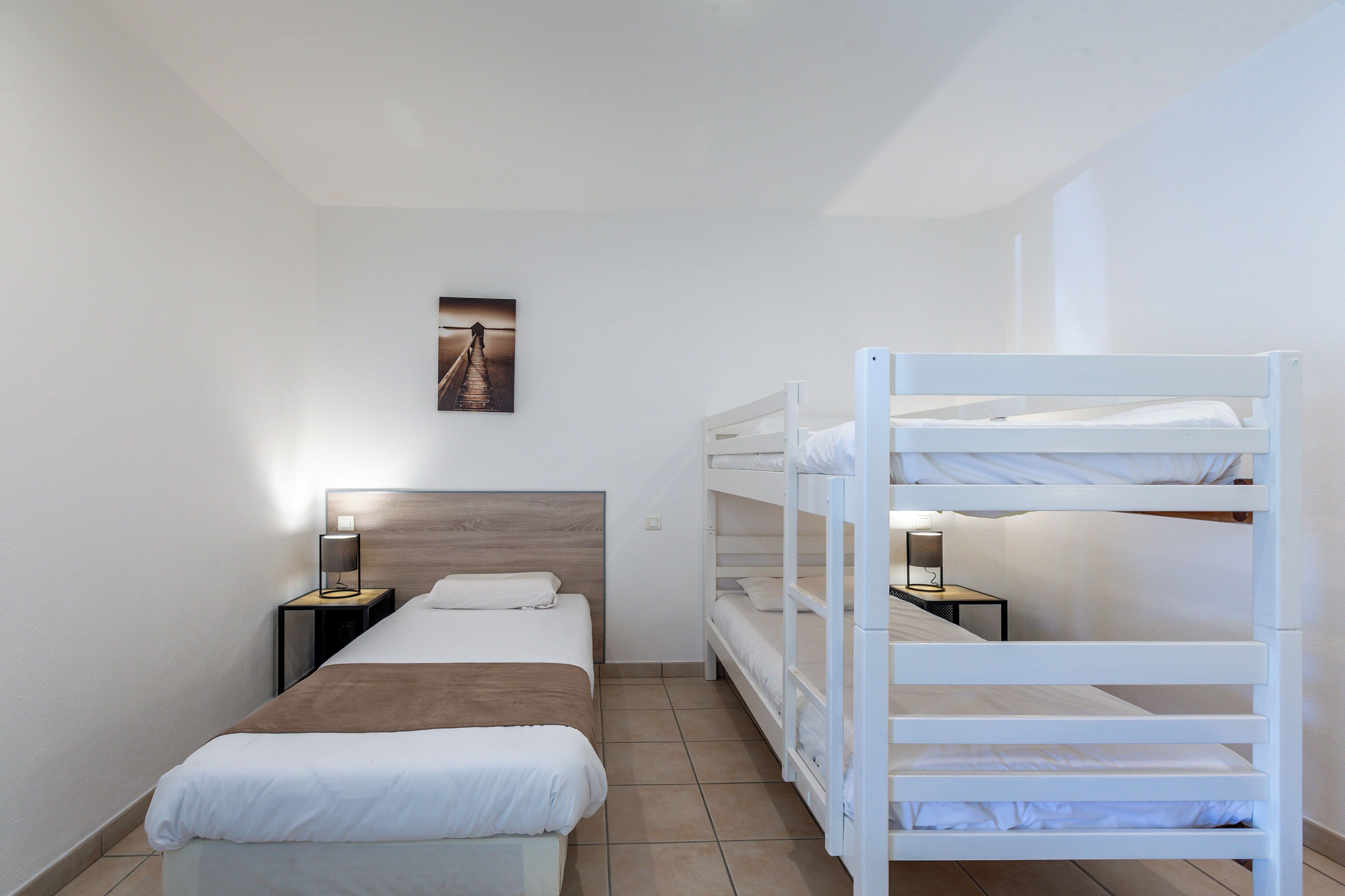 A hotel room with a single bed, a bunk bed, and a nightstand with a lamp.