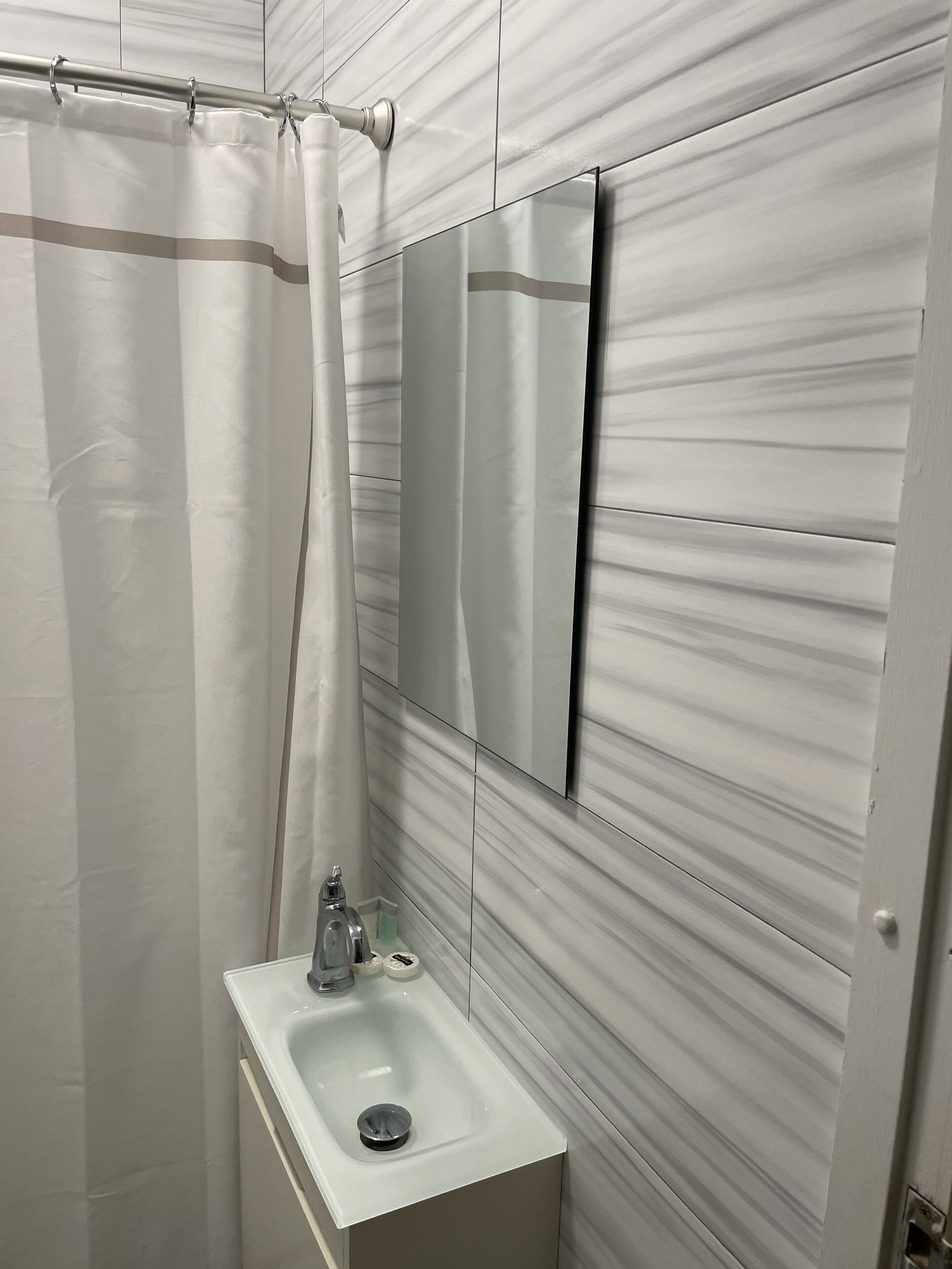 A bathroom with a shower curtain, a sink, and a mirror.