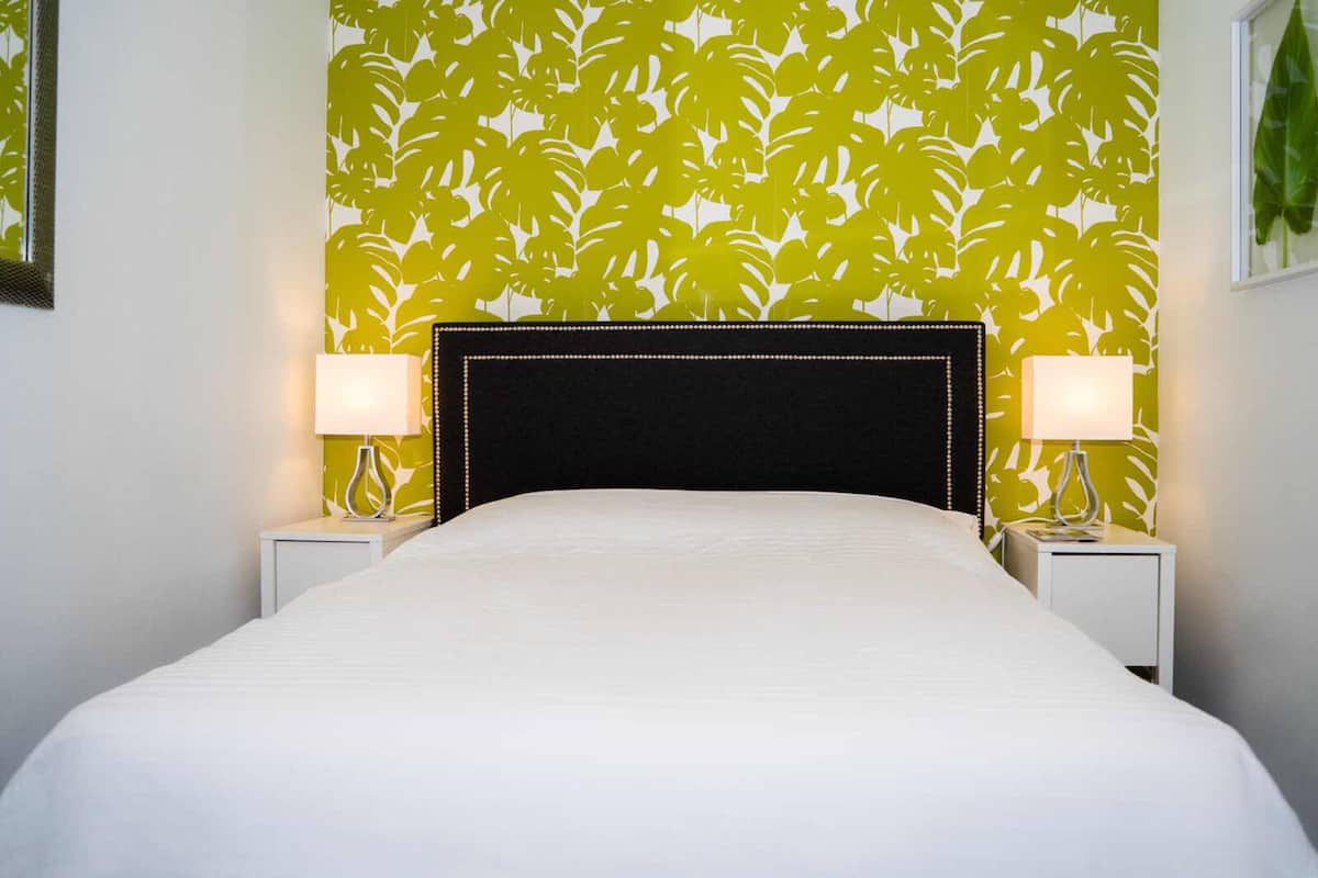 Quarto de hotel com uma cama, duas mesas de cabeceira com abajures e uma parede com padrão de folhas.