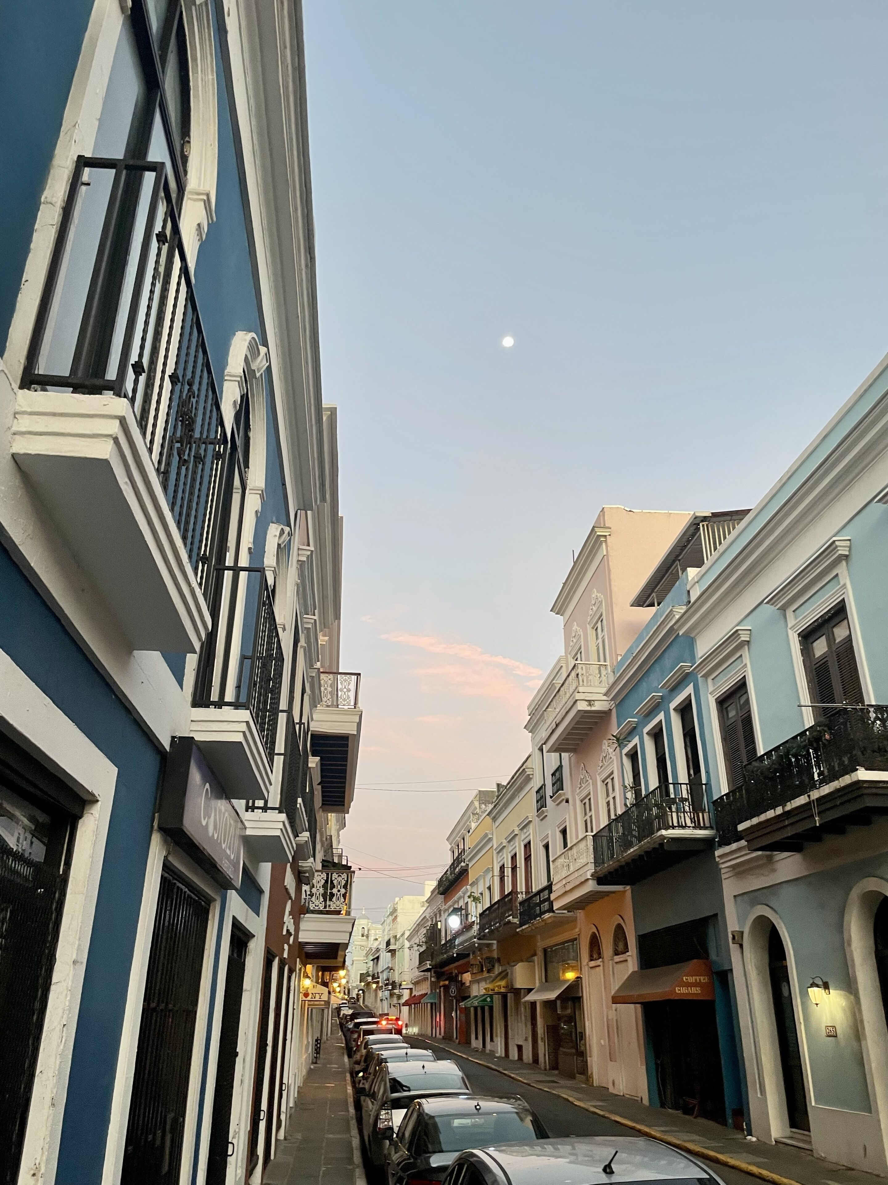 A narrow street lined with multi-story buildings, featuring balconies and storefronts.