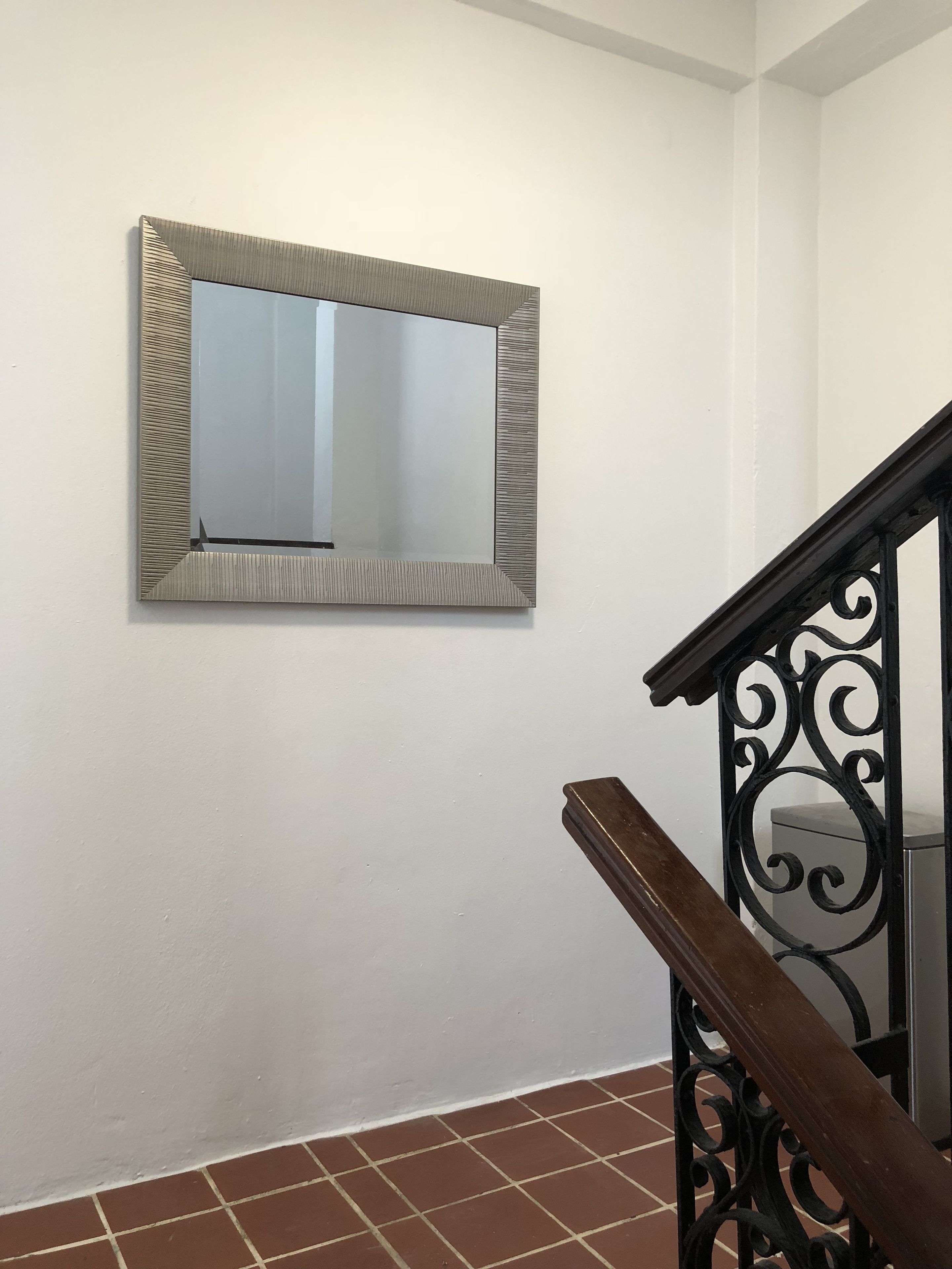 Eine Treppe mit schwarzem schmiedeeisernen Geländer und einem Wandspiegel mit strukturierter Rahmung.
