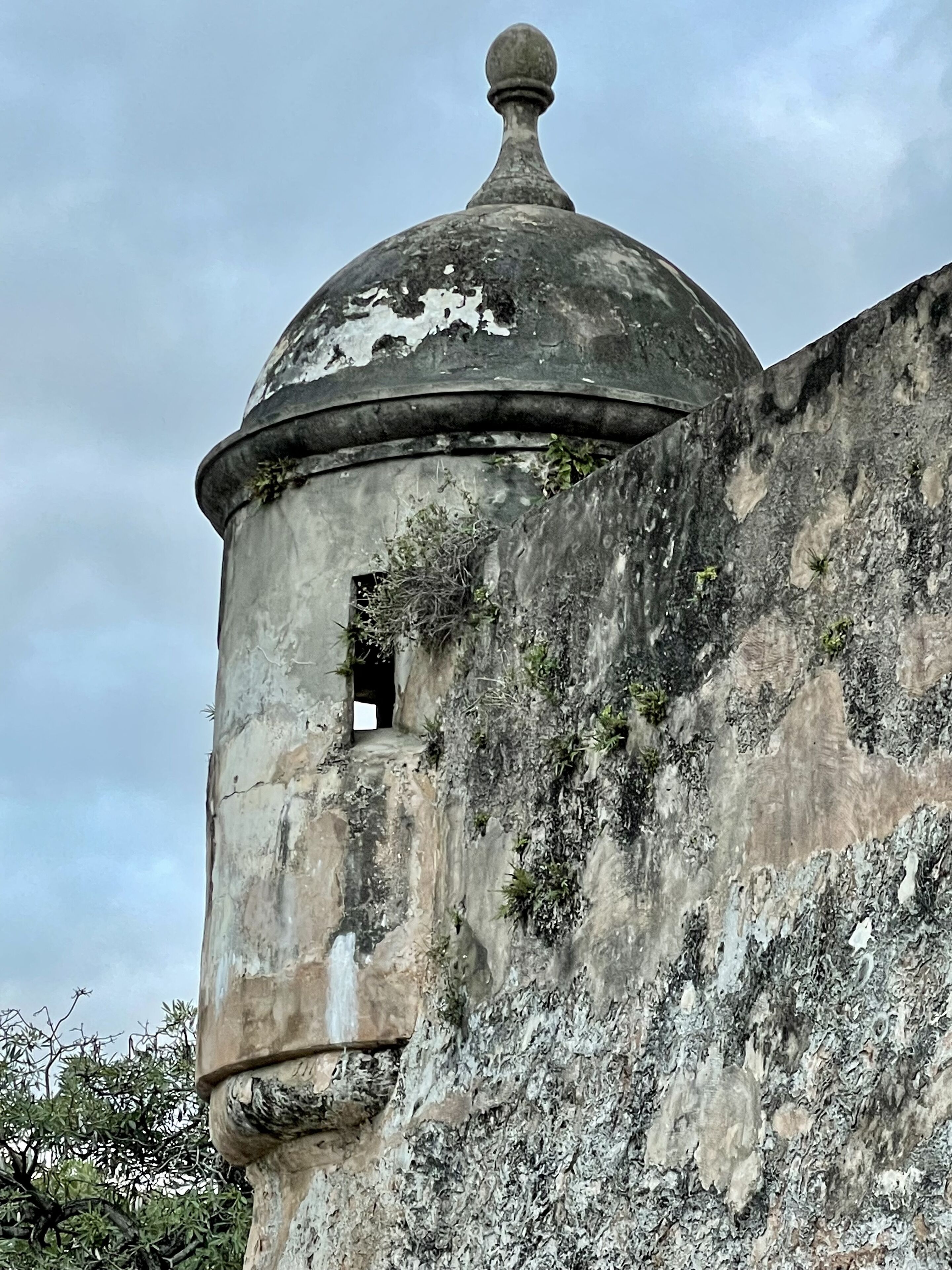 A weathered stone tower with a dome and a small window.