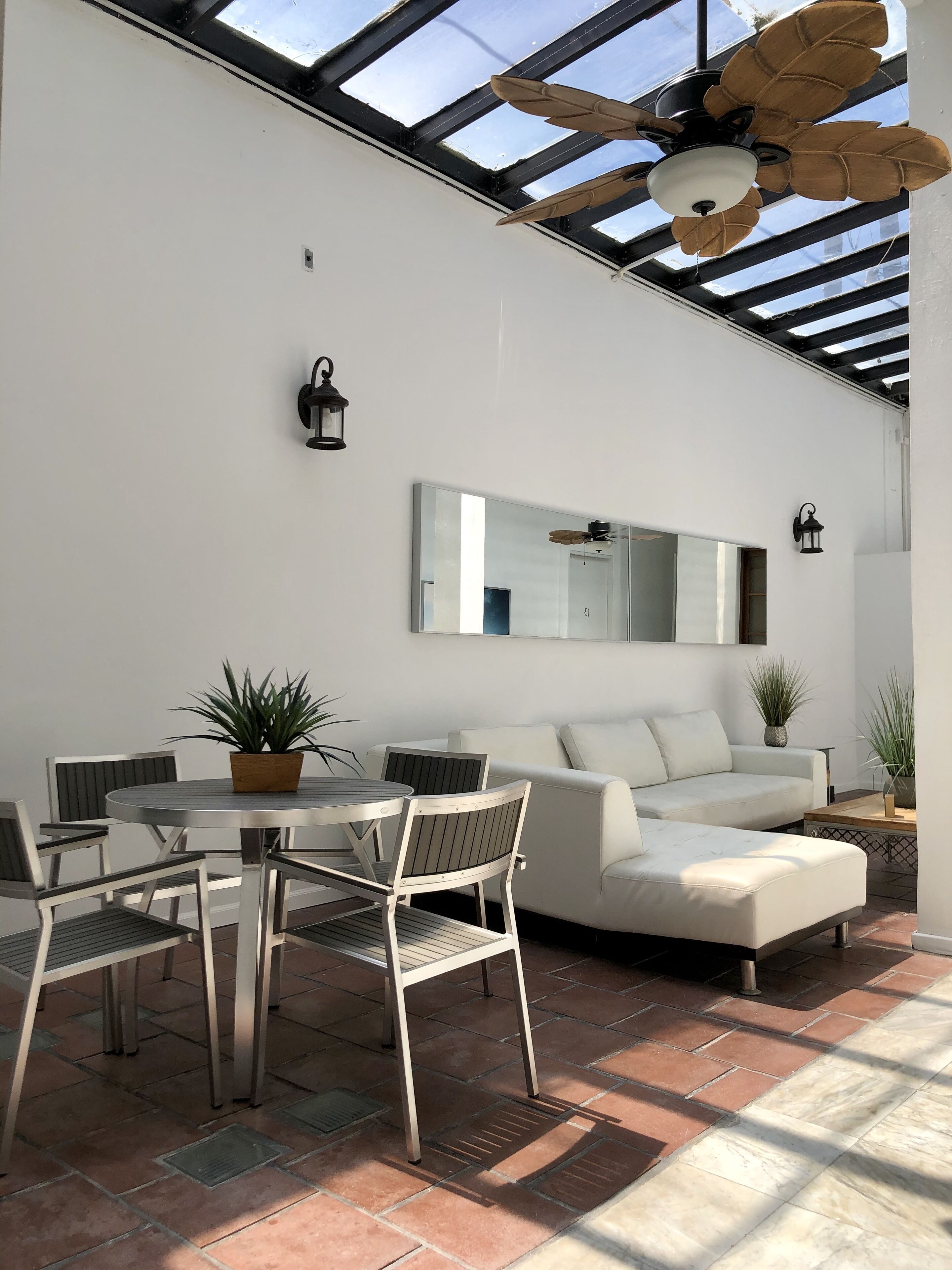 A sunlit patio with a round table, chairs, a sofa, and potted plants.