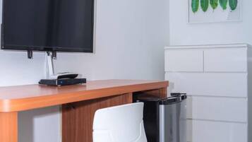 A kitchenette with a black refrigerator, a white chair, a wooden countertop, and a flat-screen TV mounted on the wall.