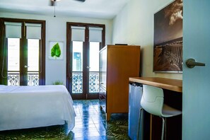 A hotel room with a bed, a desk, a chair, a refrigerator, and a balcony with a view. - Navona Studios (San Juan)