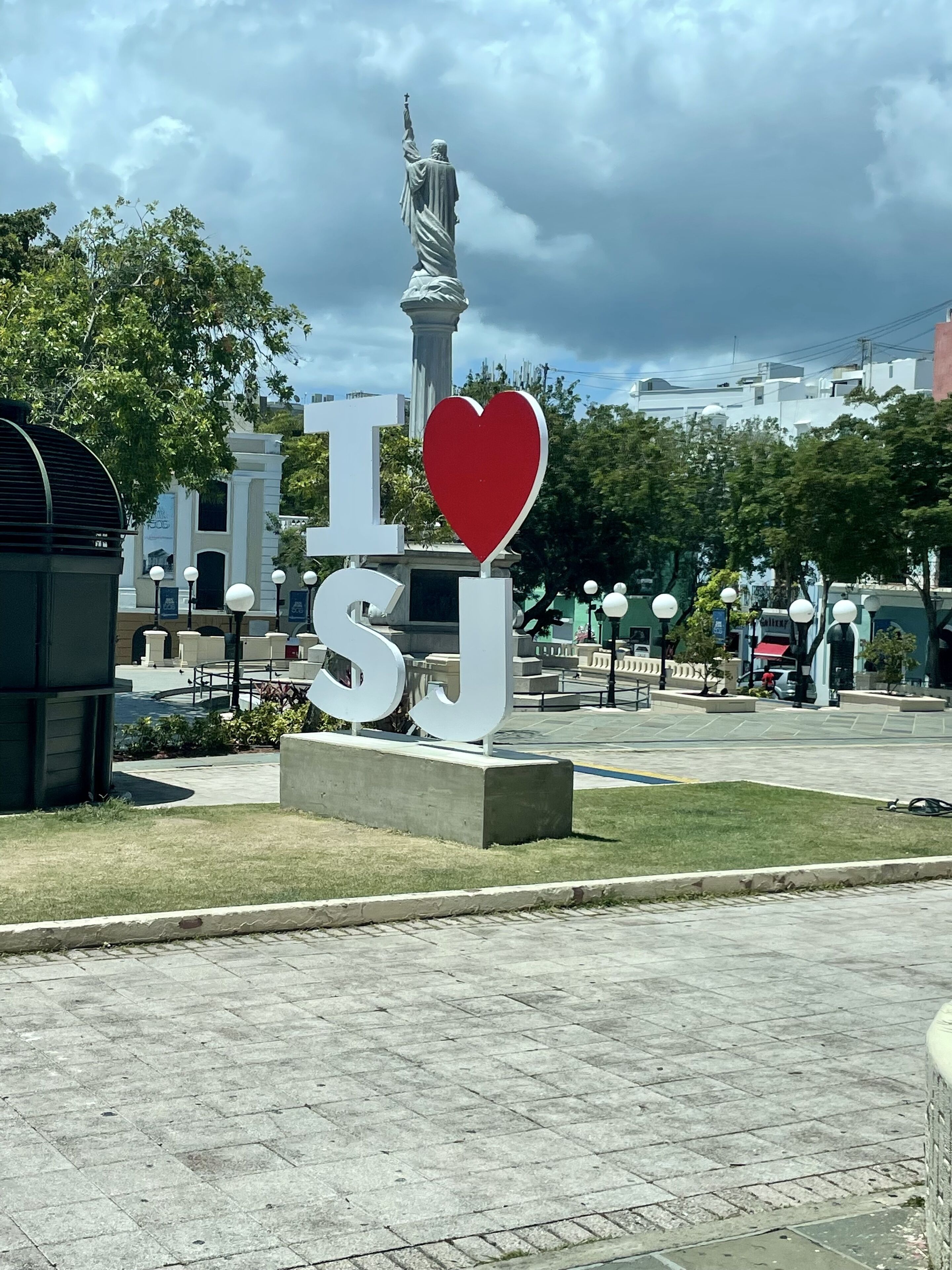 A public square with a statue, a large 'I ♥ SUJ' sign, and surrounding greenery.