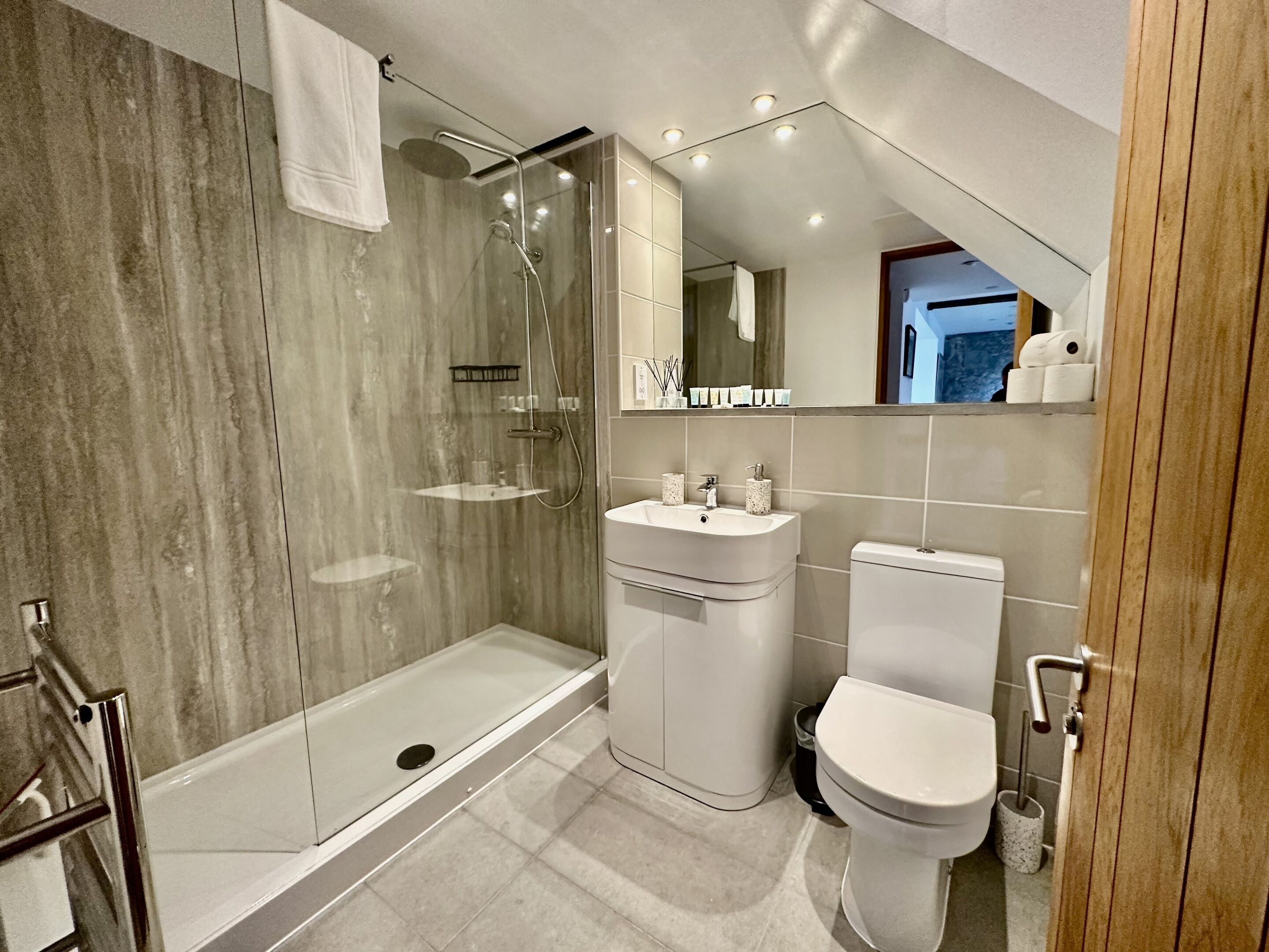 Un baño moderno con ducha de vidrio, lavamanos blanco y retrete.