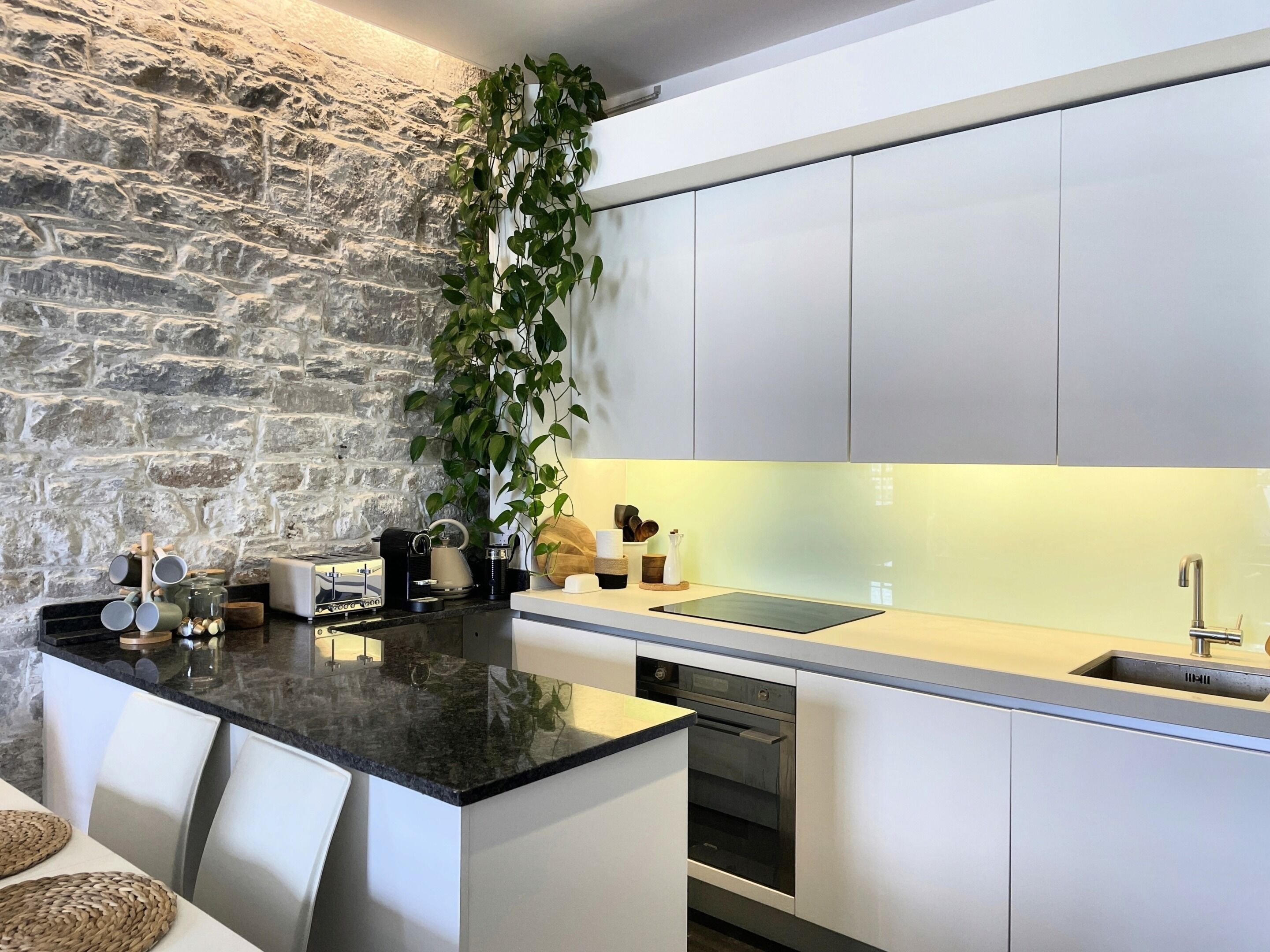 Una cocina moderna con pared de piedra, armarios blancos y una isla central con taburetes de bar.