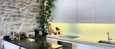 Une cuisine moderne avec un mur en pierre, des meubles blancs et un îlot central doté de tabourets de bar.