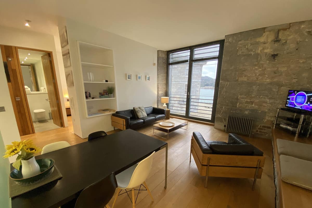 Un salon moderne avec un coin repas, de grandes fenêtres et un mur en pierre.