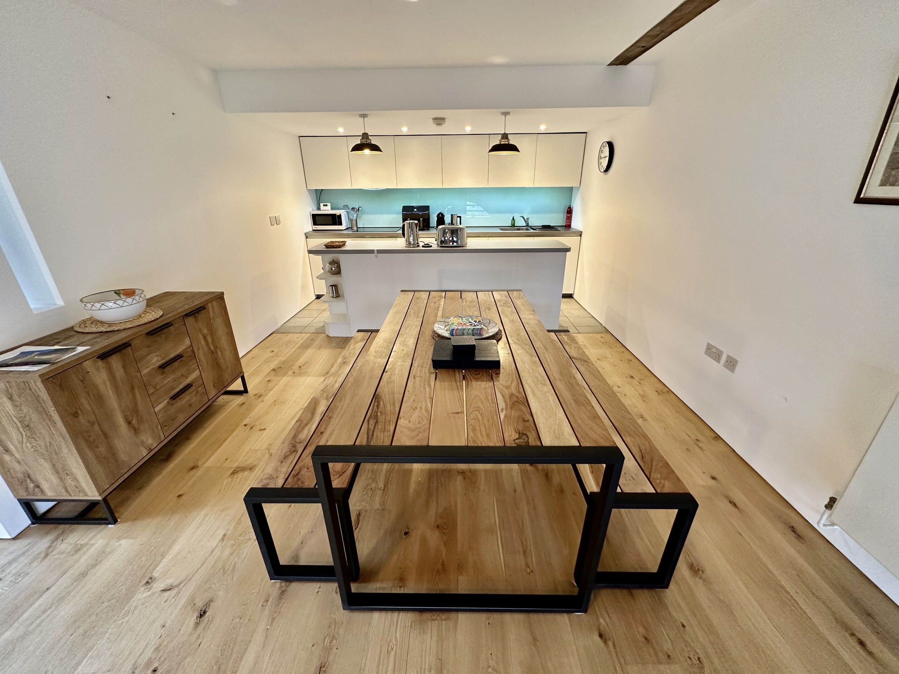 Una cocina moderna con una isla central, suelo de madera e iluminación colgante.