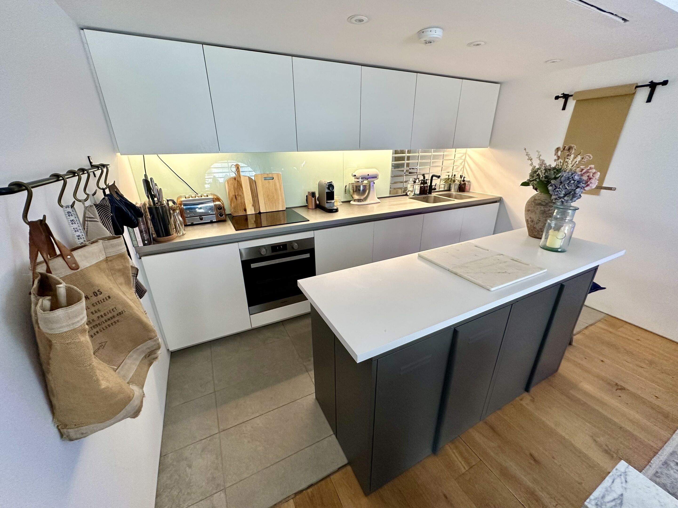 A modern kitchen with white cabinets, a central island, and a hanging rack with bags.