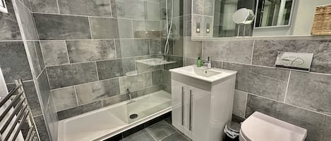 Et moderne badeværelse med en glasafskærmet bruseniche, en hvid vask og et toilet.