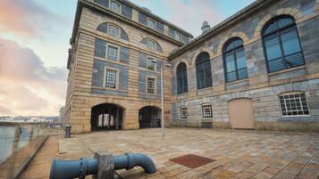 Un grand bâtiment en pierre, doté de nombreuses fenêtres en arc de cercle et d’une entrée centrale.