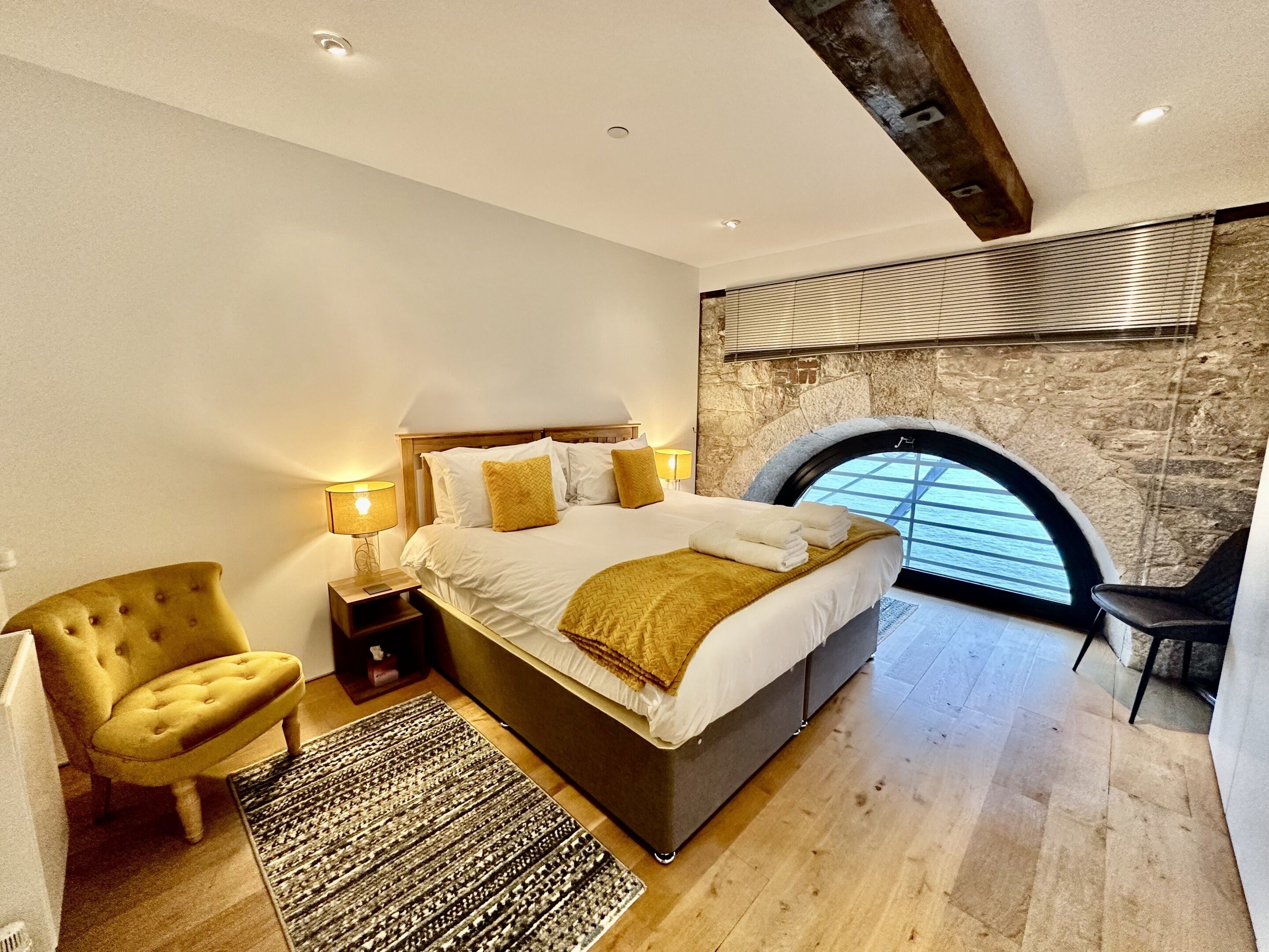A modern bedroom with a large bed, a stone wall, and a skylight.