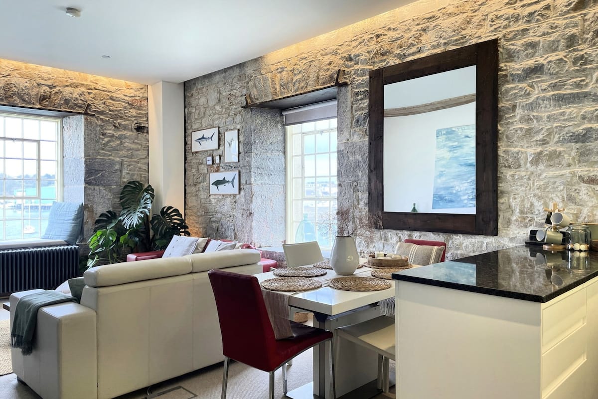 Un salon moderne avec un mur en pierre, une grande fenêtre, un canapé blanc, une table à manger et un coin cuisine.