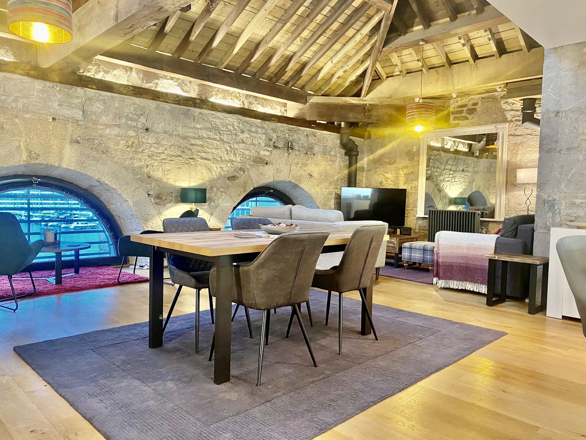 Un interior acogedor y rústico con pared de piedra, techo de madera y zona de comedor con una mesa y sillas.