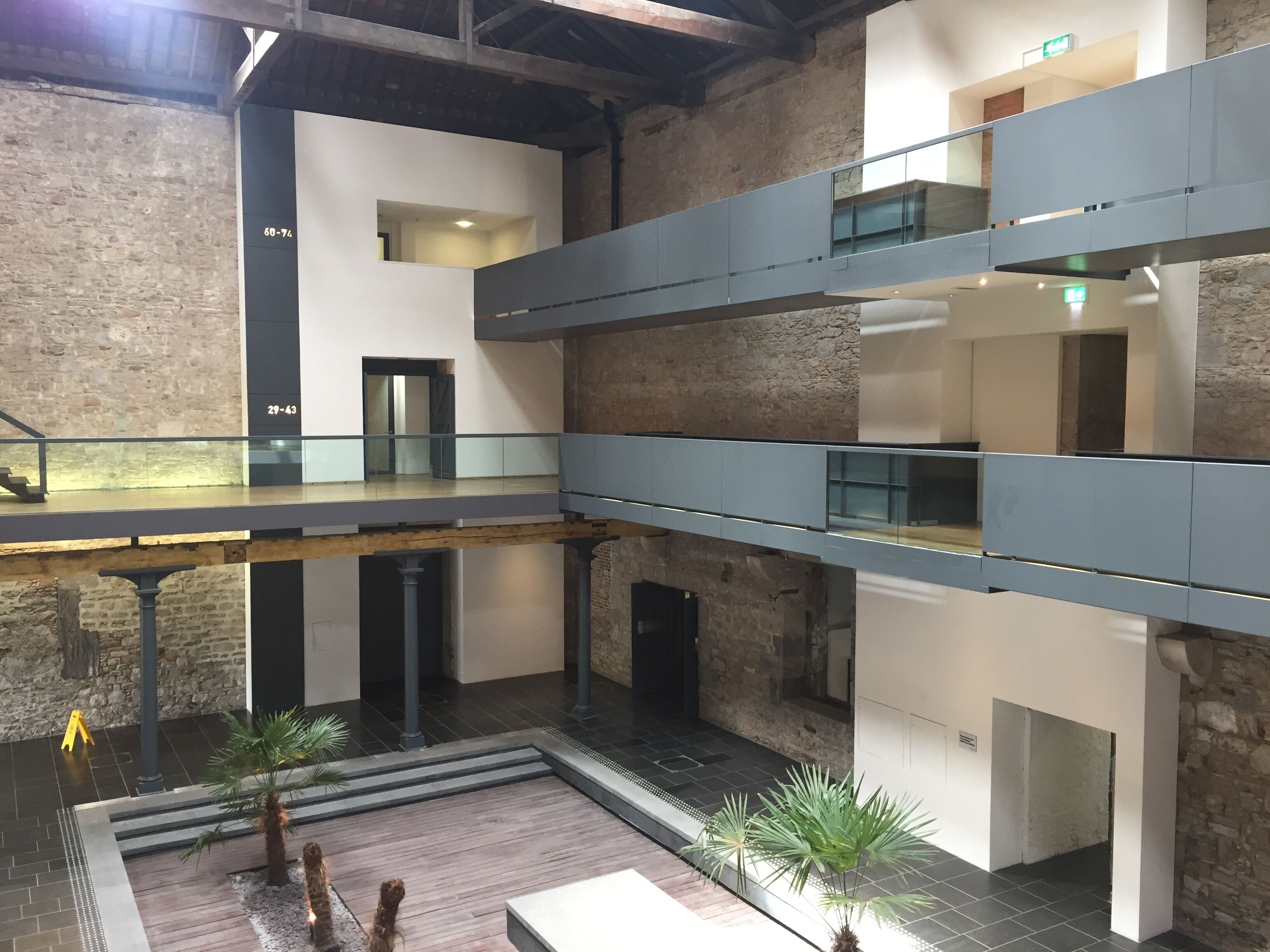 A multi-level interior with exposed brick walls, a central courtyard with plants, and a modern design with glass railings.