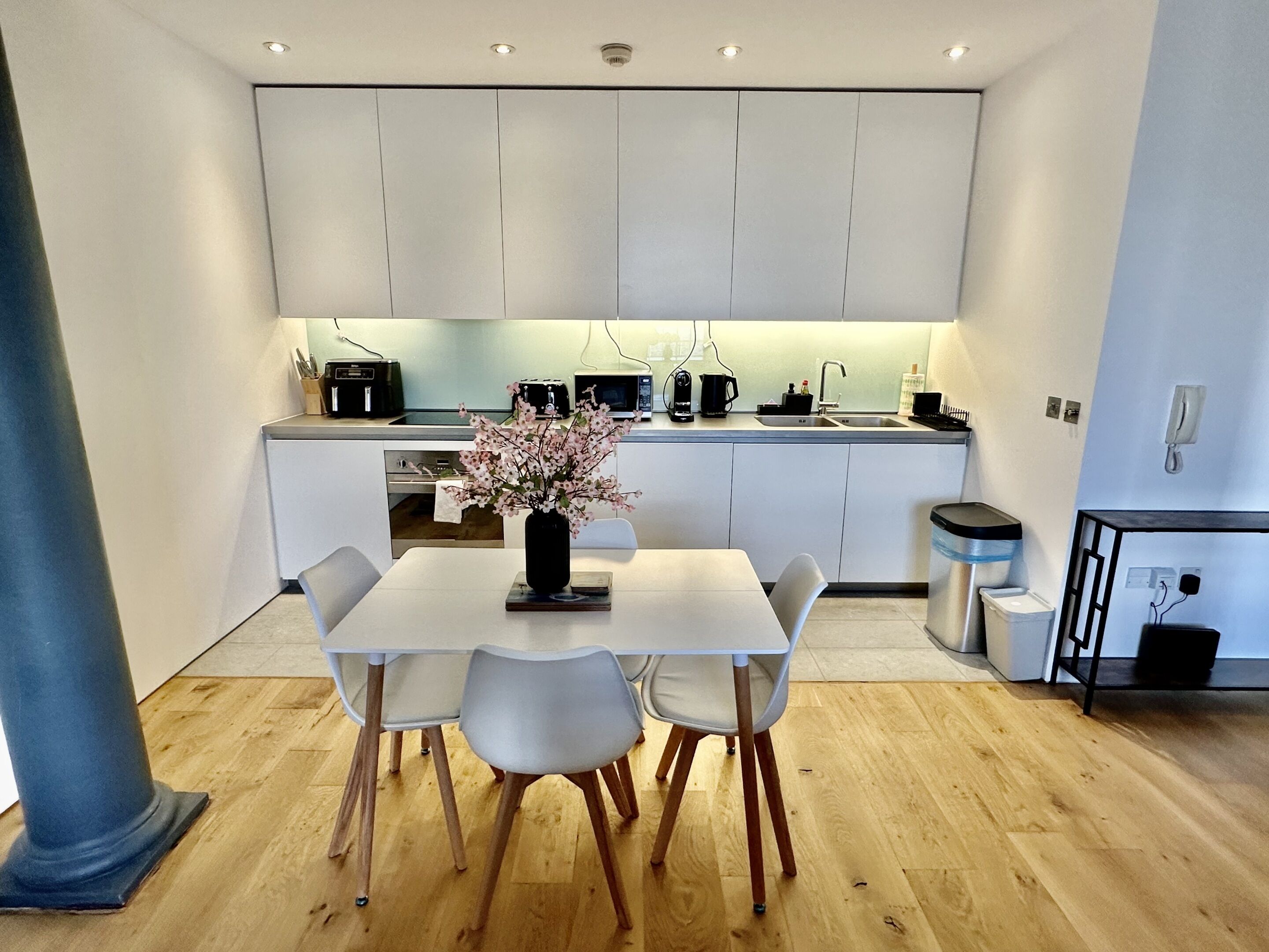 Una cocina moderna con armarios blancos, una mesa de comedor con sillas y un florero con flores.