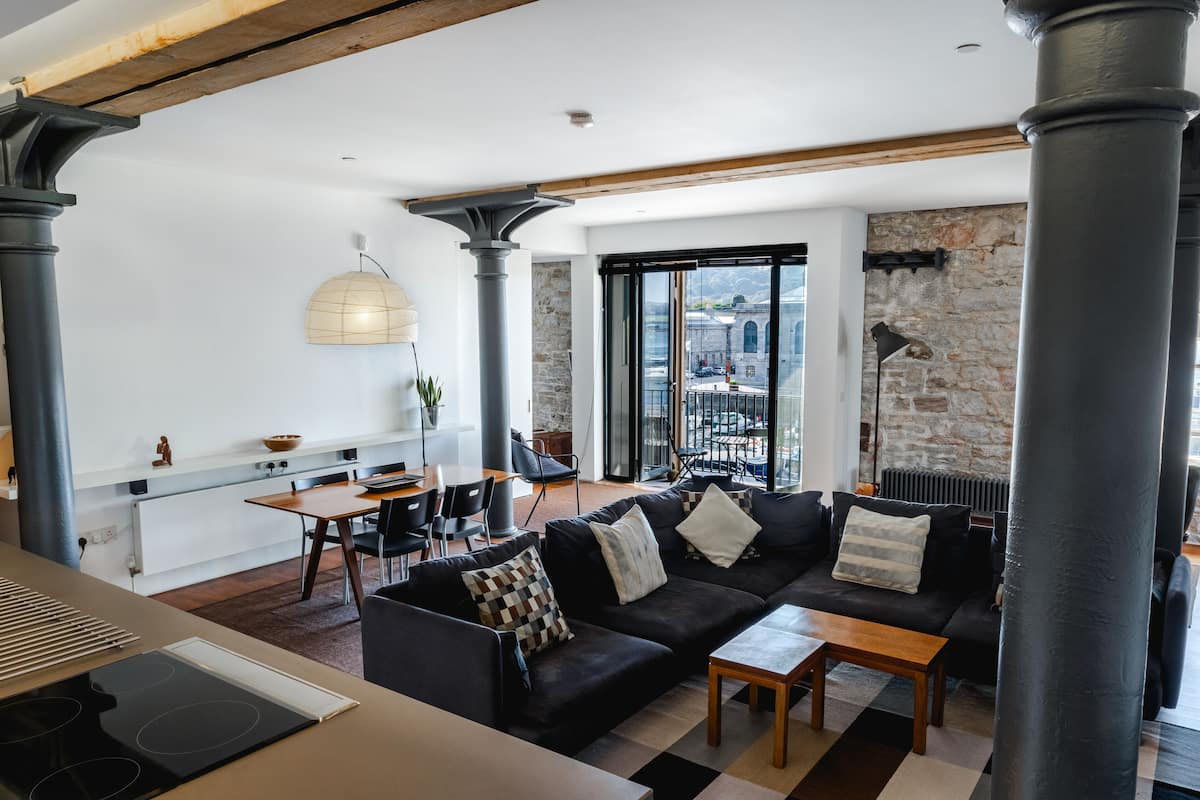 Un salon moderne avec un canapé noir, une table basse en bois et un coin repas comprenant une table et des chaises.