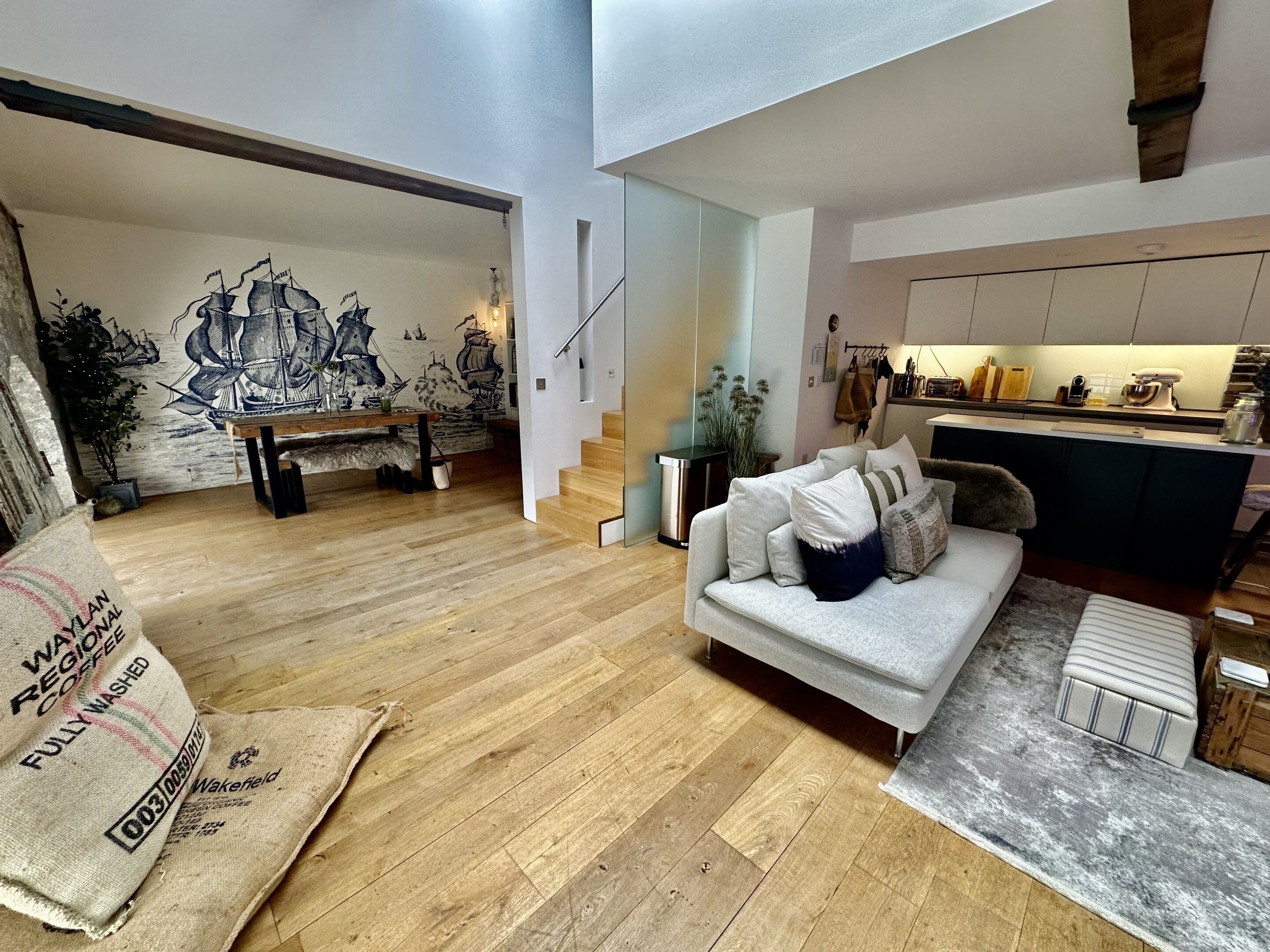 Una sala de estar moderna con piso de madera, un sofá con cojines, una mesa de centro y un mural en la pared.