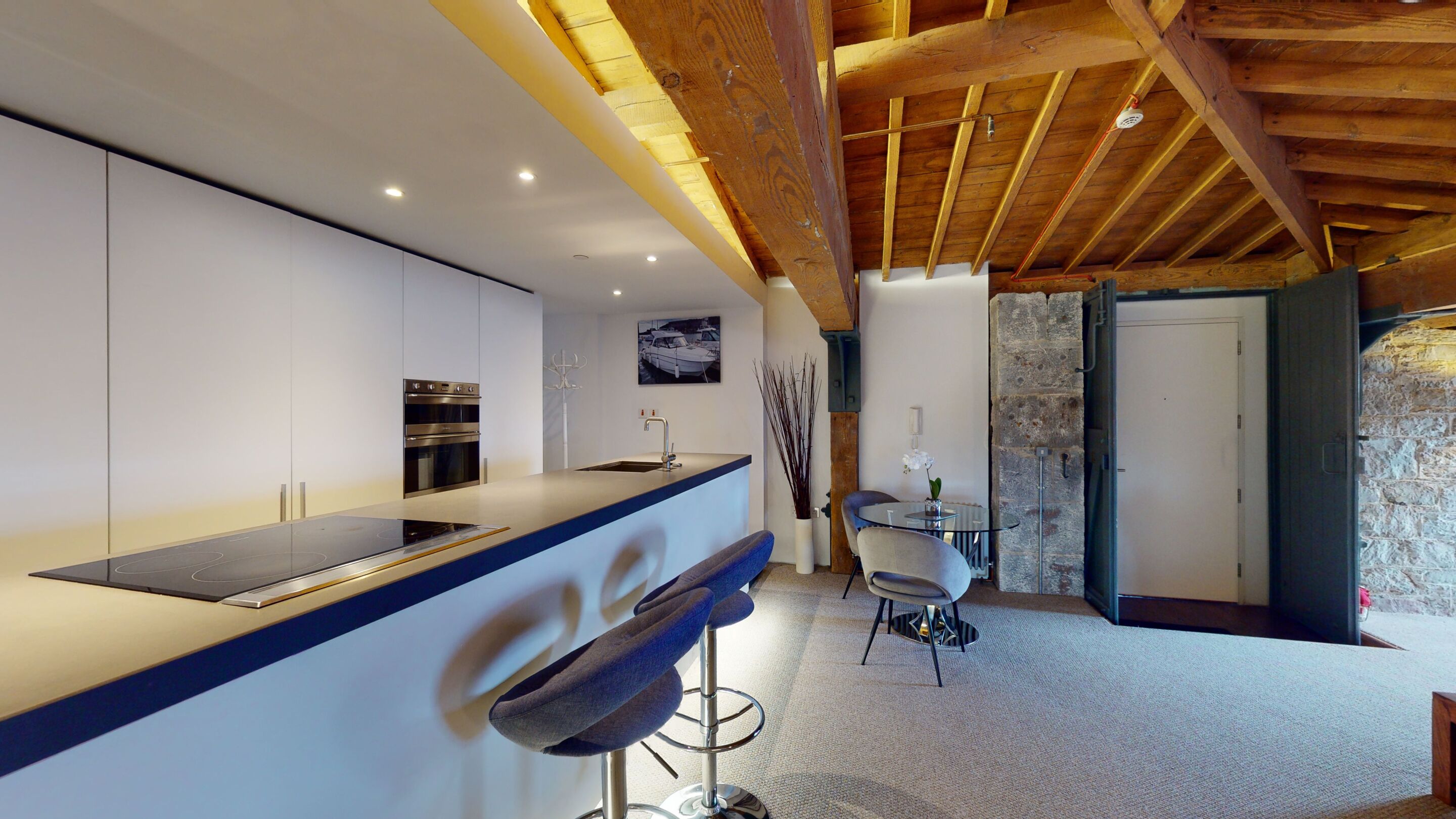 A modern kitchen with a central island, built-in oven, and a dining area with a round table and chairs.