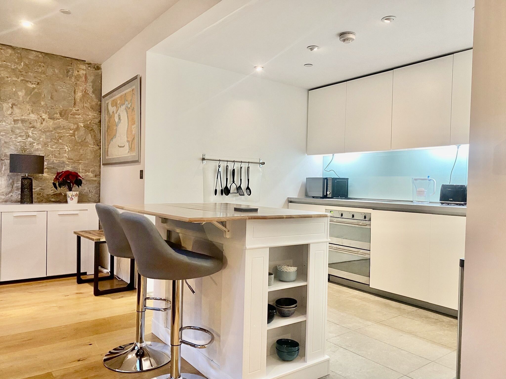 Una cocina moderna con armarios blancos, un taburete de bar y un microondas.