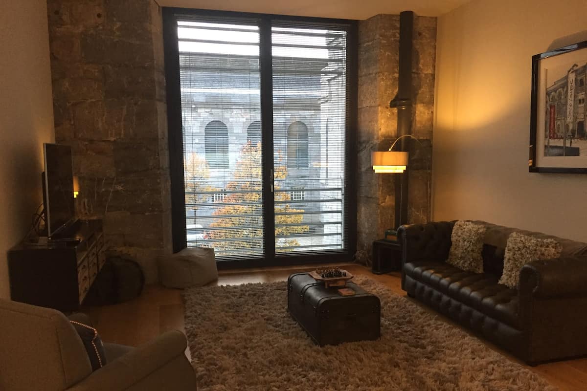 Un salon avec une grande fenêtre, une cheminée, un canapé, une table basse et une lampe.