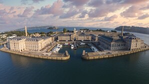 Een groot historisch gebouwencomplex met een centrale binnenplaats, omringd door water en verbonden met een haven met boten.