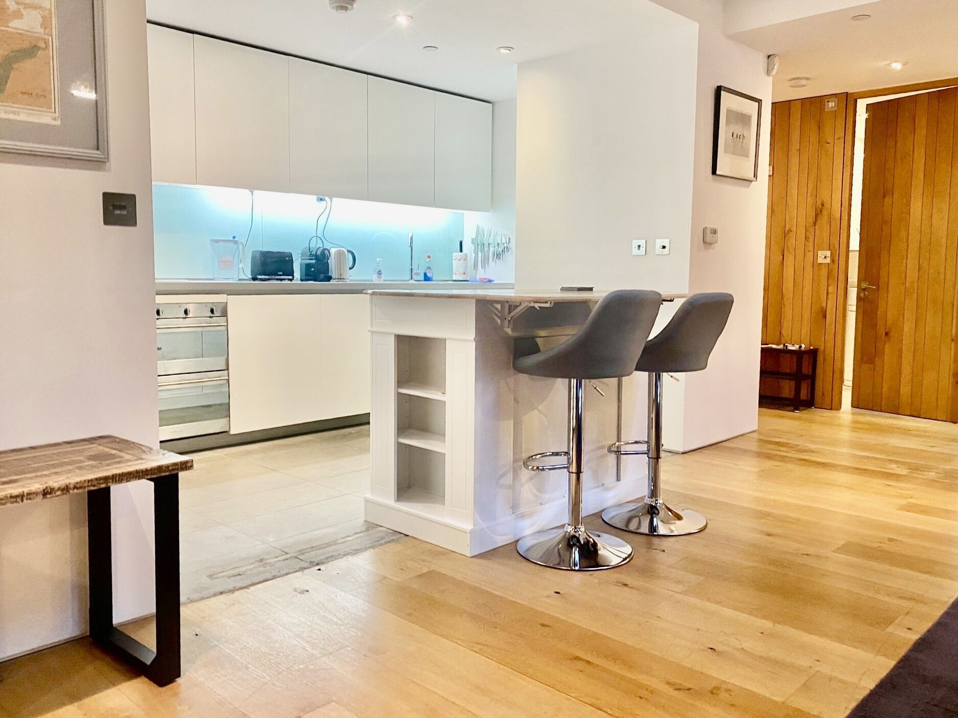 Una cocina moderna con armarios blancos, una isla central con taburetes y suelo de madera.
