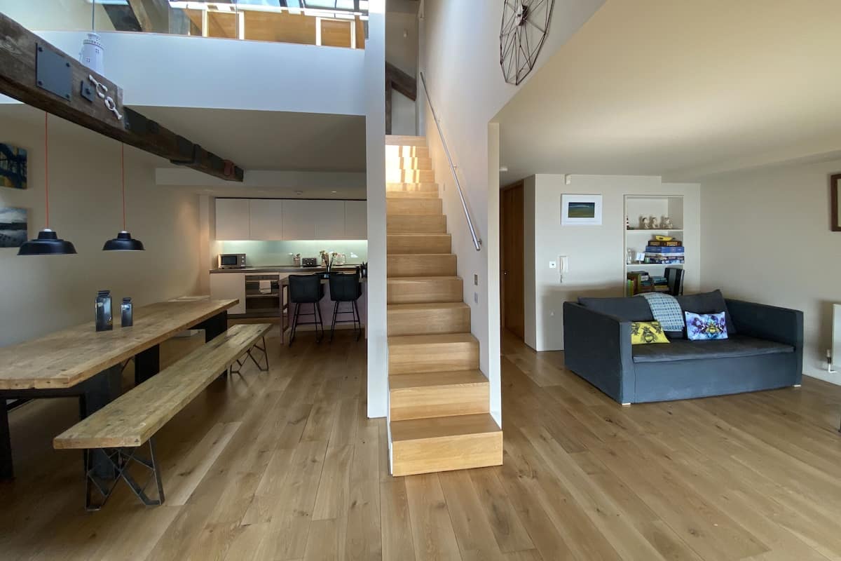 Un intérieur moderne avec un escalier en bois, un coin repas avec un banc et un salon doté d’un canapé.