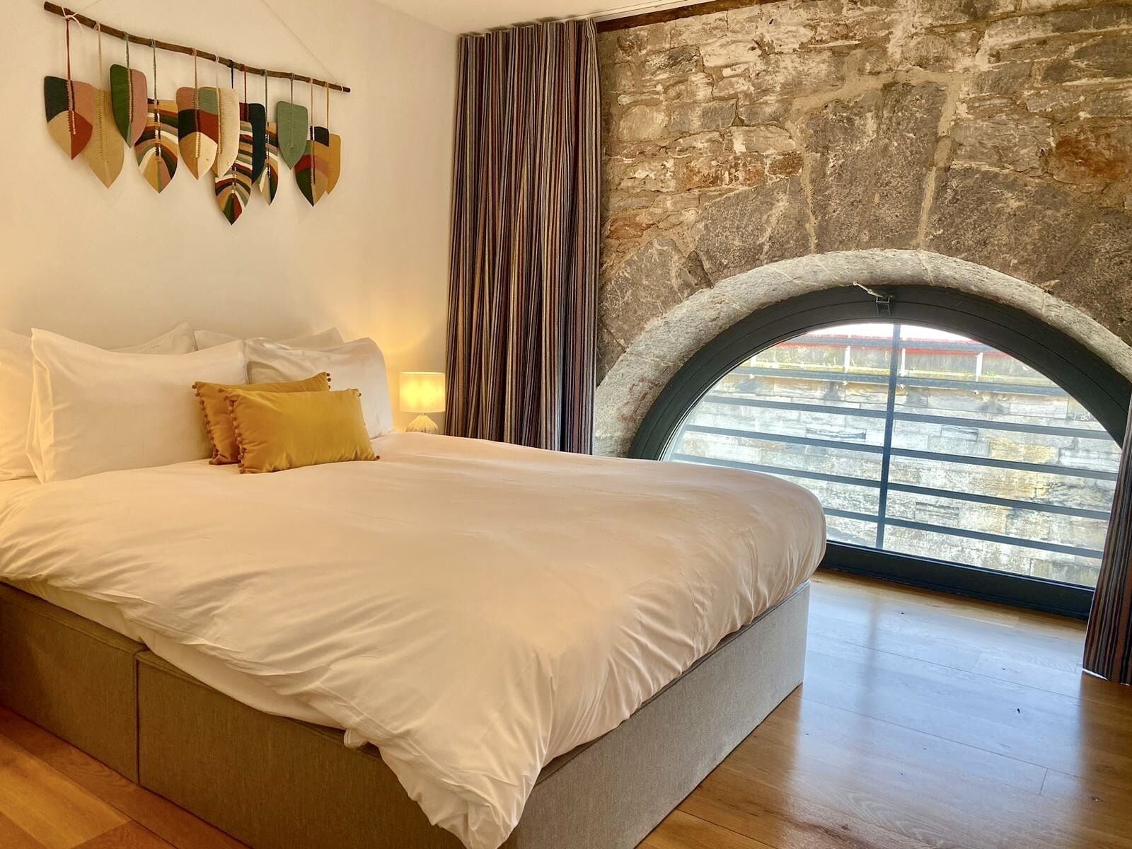 Un dormitorio con una cama grande, una pared de piedra, una ventana con vistas y una cortina.