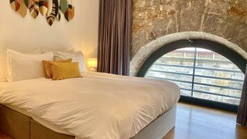 Un dormitorio con una cama grande, una pared de piedra, una ventana con vistas y una cortina.